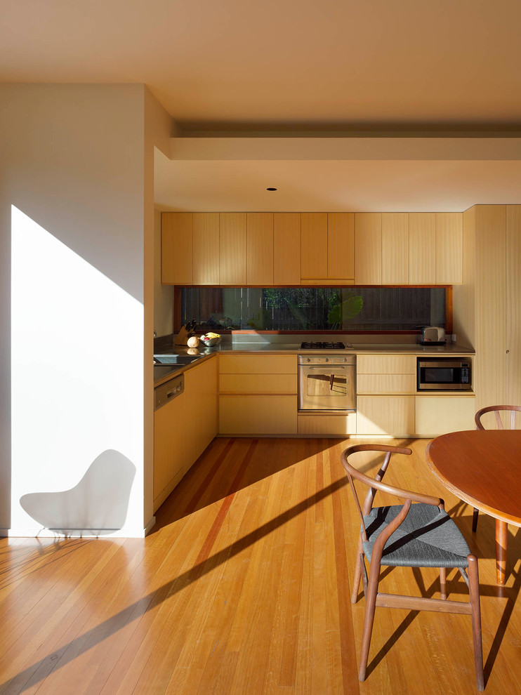 Свежая идея для дизайна: угловая кухня-гостиная в современном стиле с светлыми деревянными фасадами, столешницей из нержавеющей стали, фартуком из стекла, техникой из нержавеющей стали и паркетным полом среднего тона без острова - отличное фото интерьера