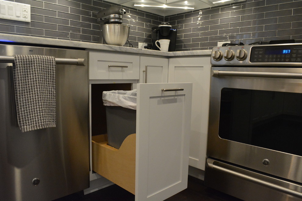 Modern inredning av ett kök och matrum, med vita skåp, granitbänkskiva, grått stänkskydd, stänkskydd i tunnelbanekakel, rostfria vitvaror och mörkt trägolv
