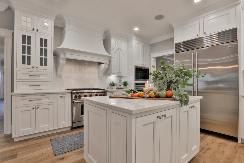 Inspiration for a large traditional u-shaped kitchen/diner in Boston with a belfast sink, beaded cabinets, white cabinets, engineered stone countertops, white splashback, marble splashback, stainless steel appliances, light hardwood flooring, an island, multi-coloured floors and white worktops.