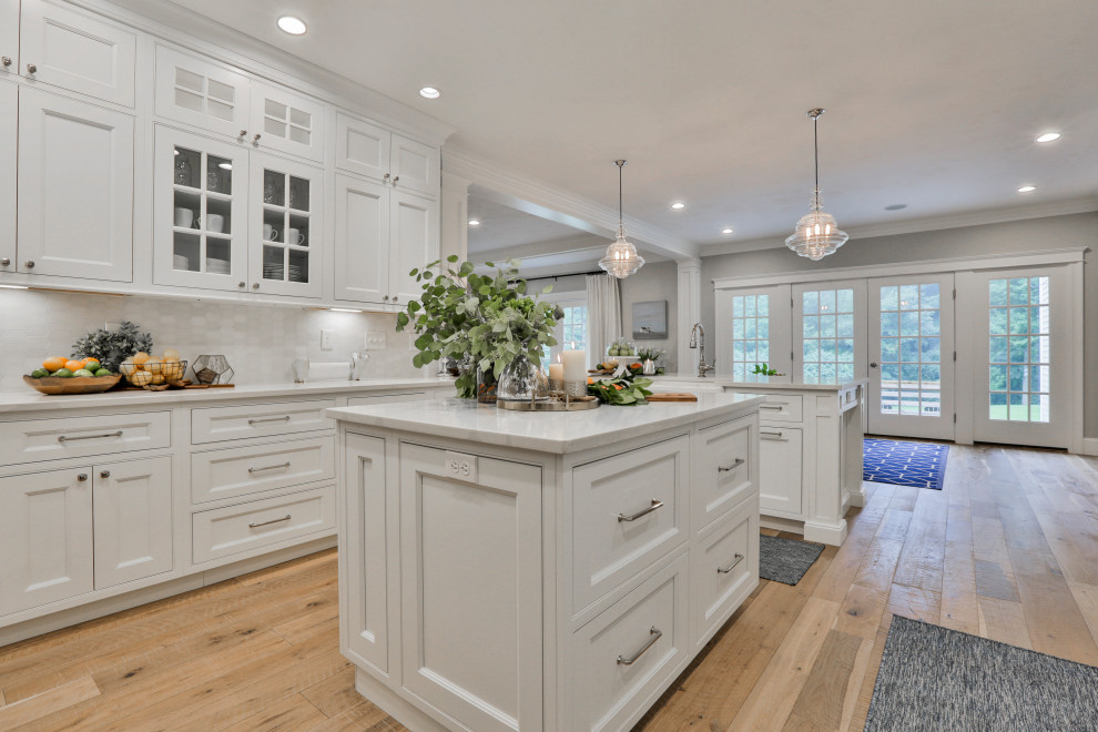 Example of a large classic u-shaped light wood floor and multicolored floor eat-in kitchen design in Boston with a farmhouse sink, beaded inset cabinets, white cabinets, quartz countertops, white backsplash, marble backsplash, stainless steel appliances, an island and white countertops