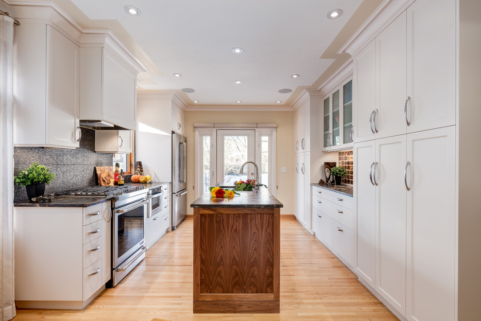 Design ideas for a traditional galley kitchen pantry in Calgary with a built-in sink, shaker cabinets, white cabinets, granite worktops, orange splashback, stainless steel appliances, light hardwood flooring and an island.
