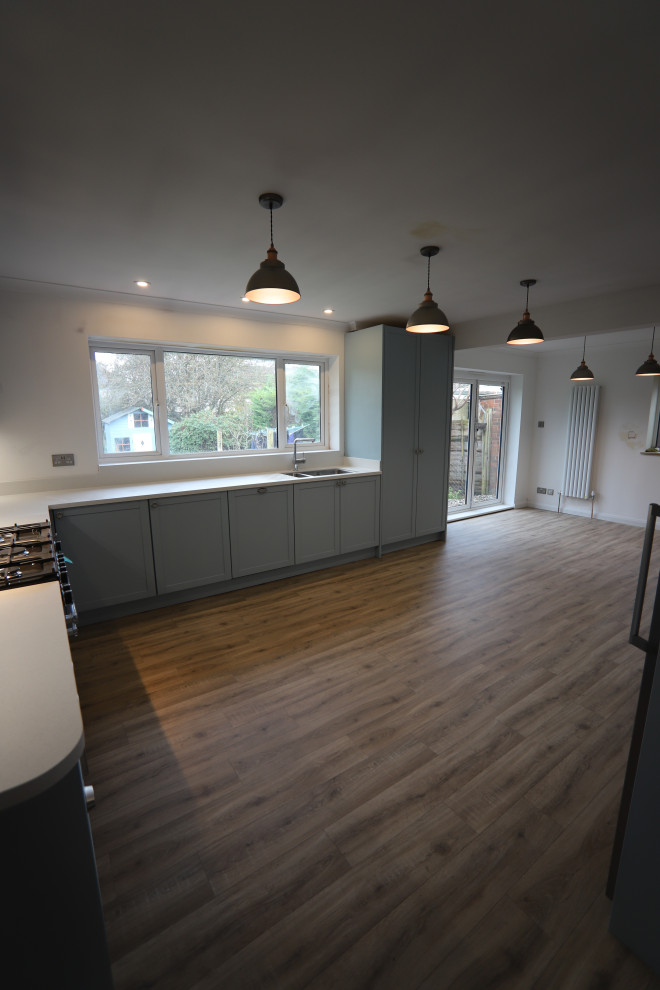Design ideas for a large contemporary u-shaped kitchen/diner in Sussex with an integrated sink, shaker cabinets, blue cabinets, composite countertops, white splashback, glass sheet splashback, stainless steel appliances, lino flooring, no island, brown floors and white worktops.
