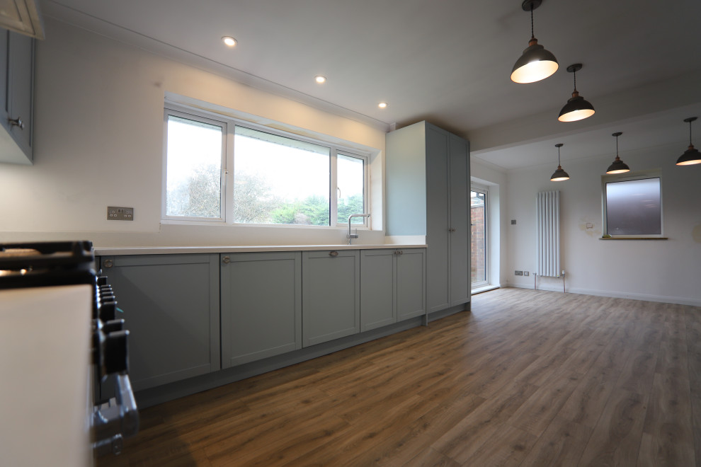 Large contemporary u-shaped kitchen/diner in Sussex with an integrated sink, shaker cabinets, blue cabinets, composite countertops, white splashback, glass sheet splashback, stainless steel appliances, lino flooring, no island, brown floors and white worktops.