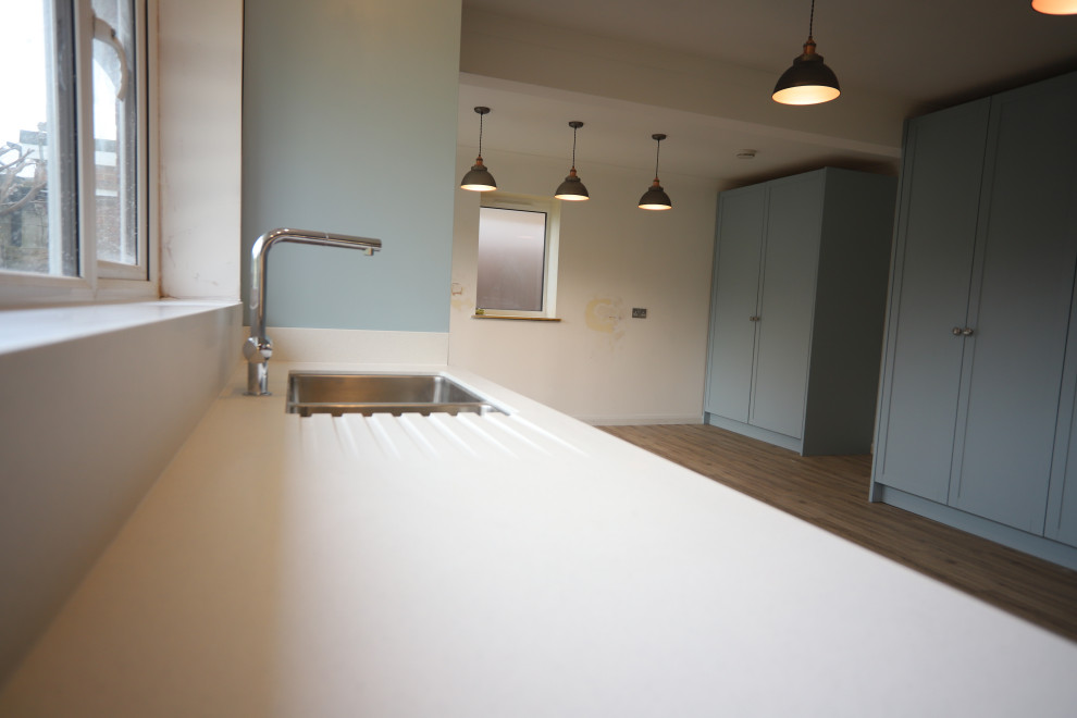 Inspiration for a large contemporary u-shaped kitchen/diner in Sussex with an integrated sink, shaker cabinets, blue cabinets, composite countertops, white splashback, glass sheet splashback, stainless steel appliances, lino flooring, no island, brown floors and white worktops.