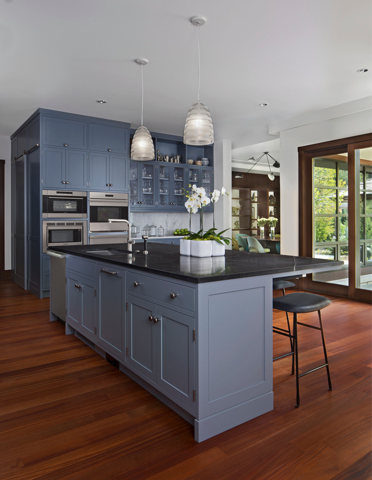 Idéer för mellanstora vintage linjära svart kök med öppen planlösning, med en undermonterad diskho, luckor med upphöjd panel, blå skåp, vitt stänkskydd, stänkskydd i sten, rostfria vitvaror, mellanmörkt trägolv, en köksö, marmorbänkskiva och brunt golv