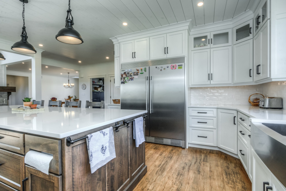 トロントにある高級な広いカントリー風のおしゃれなキッチン (エプロンフロントシンク、シェーカースタイル扉のキャビネット、白いキャビネット、クオーツストーンカウンター、白いキッチンパネル、セメントタイルのキッチンパネル、シルバーの調理設備、無垢フローリング、マルチカラーの床、白いキッチンカウンター、塗装板張りの天井) の写真