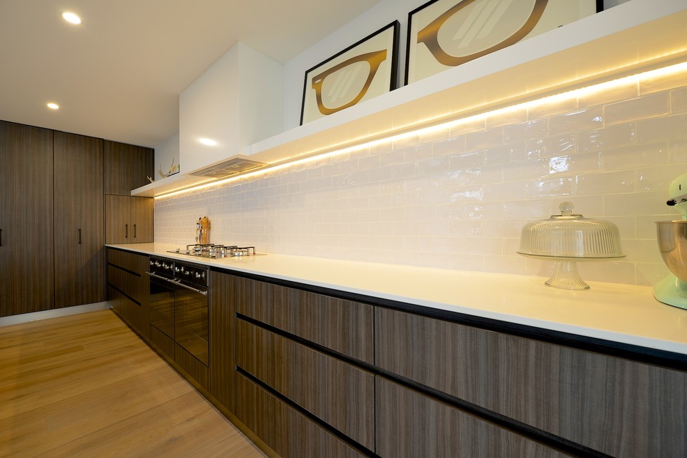 Example of a large trendy galley medium tone wood floor eat-in kitchen design in Sydney with a double-bowl sink, flat-panel cabinets, dark wood cabinets, quartz countertops, white backsplash, subway tile backsplash, stainless steel appliances and an island