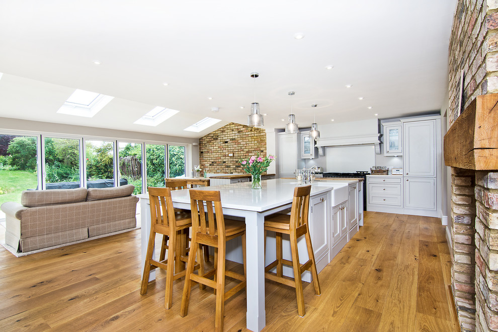 Design ideas for a large country u-shaped kitchen in Hertfordshire with a belfast sink, shaker cabinets, grey cabinets, quartz worktops, white splashback, integrated appliances, light hardwood flooring, an island and white worktops.
