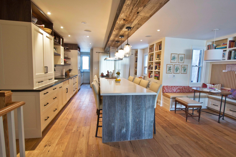 Example of a mid-sized country galley light wood floor eat-in kitchen design in Toronto with white cabinets, white backsplash, subway tile backsplash, an island, an undermount sink, beaded inset cabinets, quartz countertops and paneled appliances
