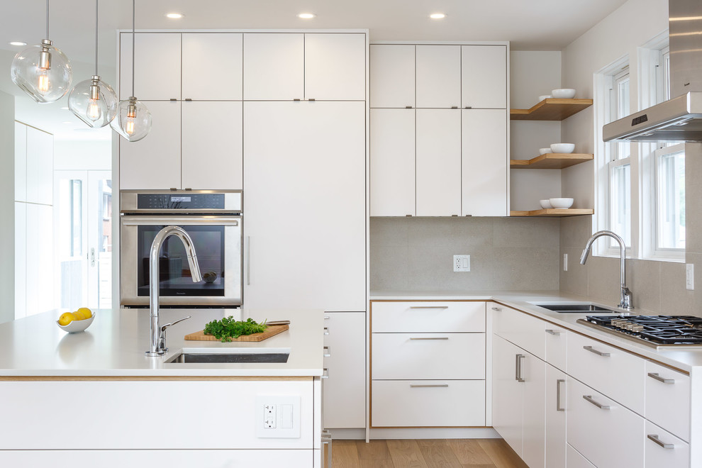 Example of a mid-sized minimalist l-shaped light wood floor and beige floor eat-in kitchen design in Ottawa with an undermount sink, flat-panel cabinets, white cabinets, solid surface countertops, beige backsplash, porcelain backsplash, stainless steel appliances and an island