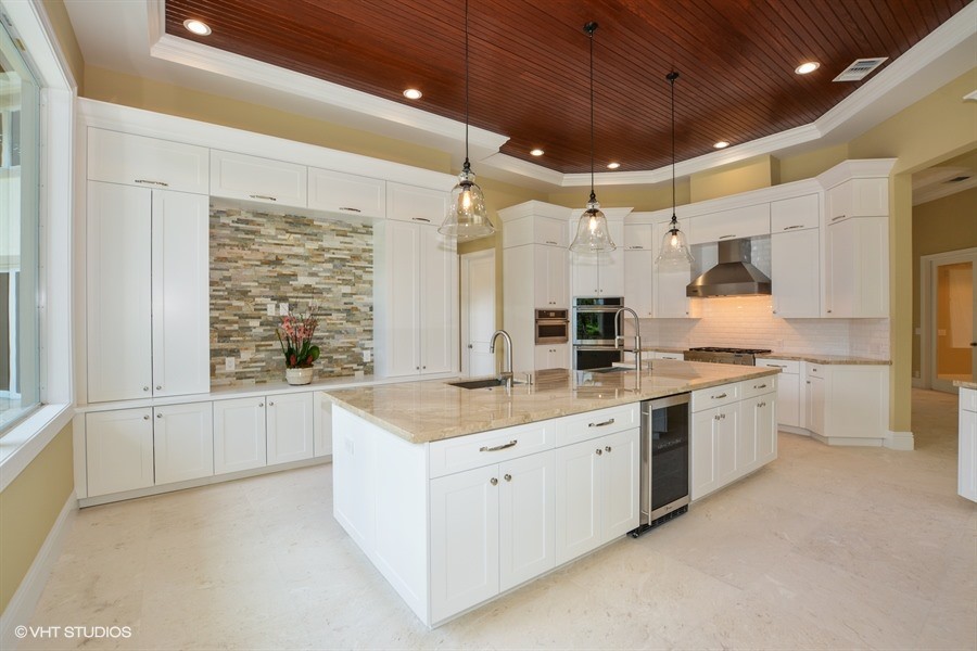 Large transitional travertine floor kitchen photo in Miami with a farmhouse sink, shaker cabinets, white cabinets, marble countertops, white backsplash, subway tile backsplash, stainless steel appliances and an island
