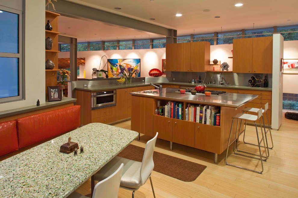 На фото: кухня в современном стиле с обеденным столом, одинарной мойкой, светлыми деревянными фасадами, столешницей из нержавеющей стали, техникой из нержавеющей стали, полом из бамбука и островом с