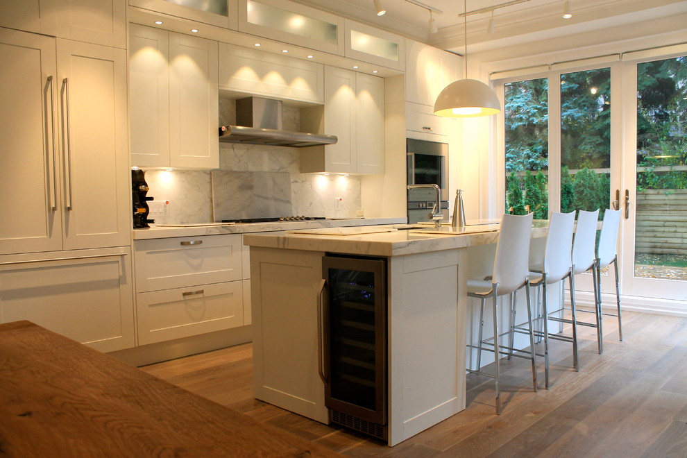 Klassisk inredning av ett linjärt kök med öppen planlösning, med en undermonterad diskho, skåp i shakerstil, vita skåp, marmorbänkskiva, vitt stänkskydd, stänkskydd i sten, rostfria vitvaror, mellanmörkt trägolv och en köksö