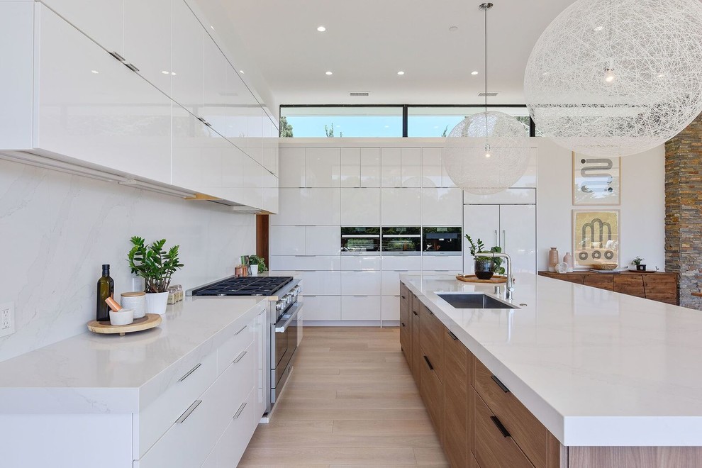 Photo of a contemporary l-shaped kitchen in San Francisco with a submerged sink, flat-panel cabinets, white cabinets, white splashback, integrated appliances, light hardwood flooring, an island, beige floors and white worktops.