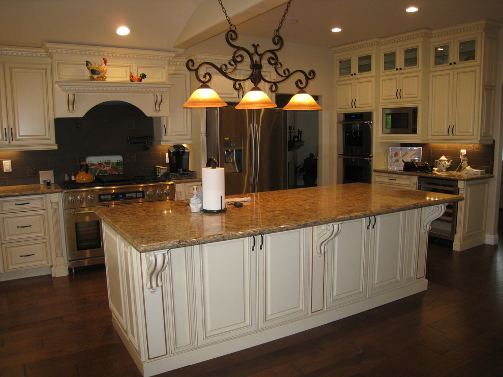Bild på ett stort funkis kök, med luckor med upphöjd panel, vita skåp, granitbänkskiva, brunt stänkskydd, stänkskydd i tunnelbanekakel, rostfria vitvaror, mörkt trägolv och en köksö