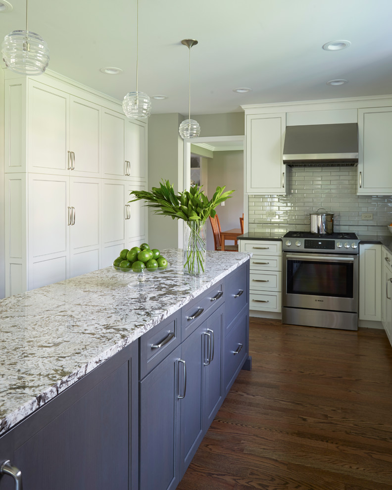 This is an example of a medium sized traditional galley kitchen/diner in Chicago with white cabinets, engineered stone countertops, grey splashback, stainless steel appliances, medium hardwood flooring, an island, a submerged sink, recessed-panel cabinets and glass tiled splashback.