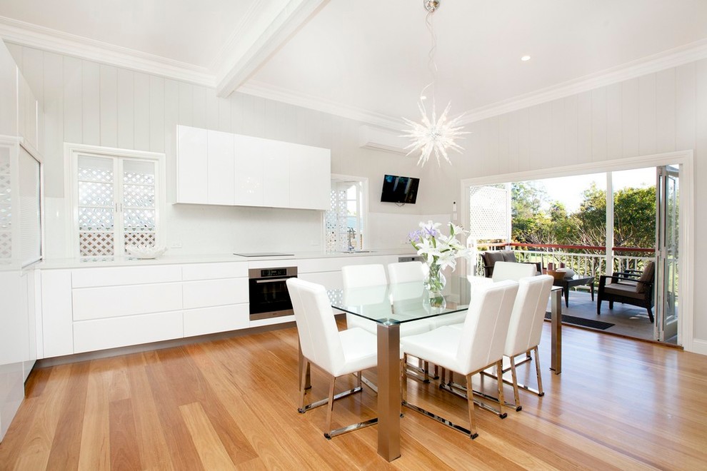 Photo of an expansive contemporary l-shaped kitchen/diner in Brisbane with flat-panel cabinets, white cabinets, white splashback, stainless steel appliances, light hardwood flooring, no island, a double-bowl sink, composite countertops and glass sheet splashback.