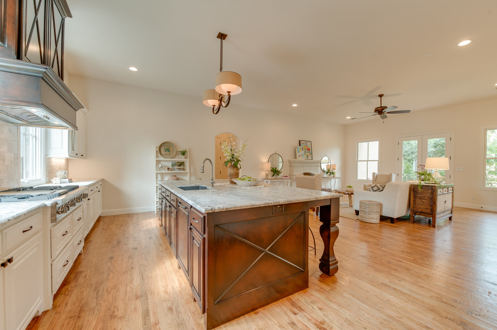 Foto på ett stort medelhavsstil kök, med en dubbel diskho, vita skåp, granitbänkskiva, grått stänkskydd, stänkskydd i tunnelbanekakel, rostfria vitvaror, ljust trägolv och en köksö