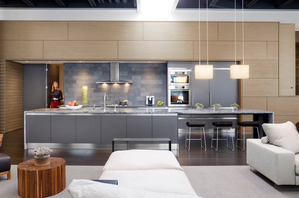 Свежая идея для дизайна: параллельная кухня-гостиная в современном стиле с плоскими фасадами, серыми фасадами, серым фартуком, техникой под мебельный фасад и фартуком из каменной плитки - отличное фото интерьера