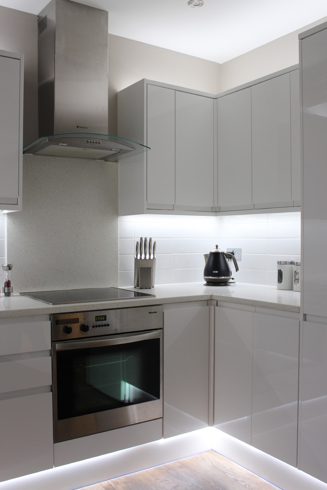 Klassisk inredning av ett avskilt, litet u-kök, med luckor med infälld panel, vita skåp, granitbänkskiva, vita vitvaror och laminatgolv