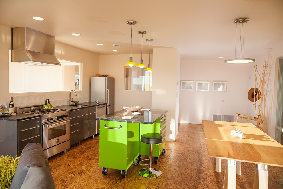 Bild på ett litet funkis linjärt kök och matrum, med en undermonterad diskho, släta luckor, grå skåp, bänkskiva i täljsten, vitt stänkskydd, stänkskydd i keramik, rostfria vitvaror, plywoodgolv och en köksö