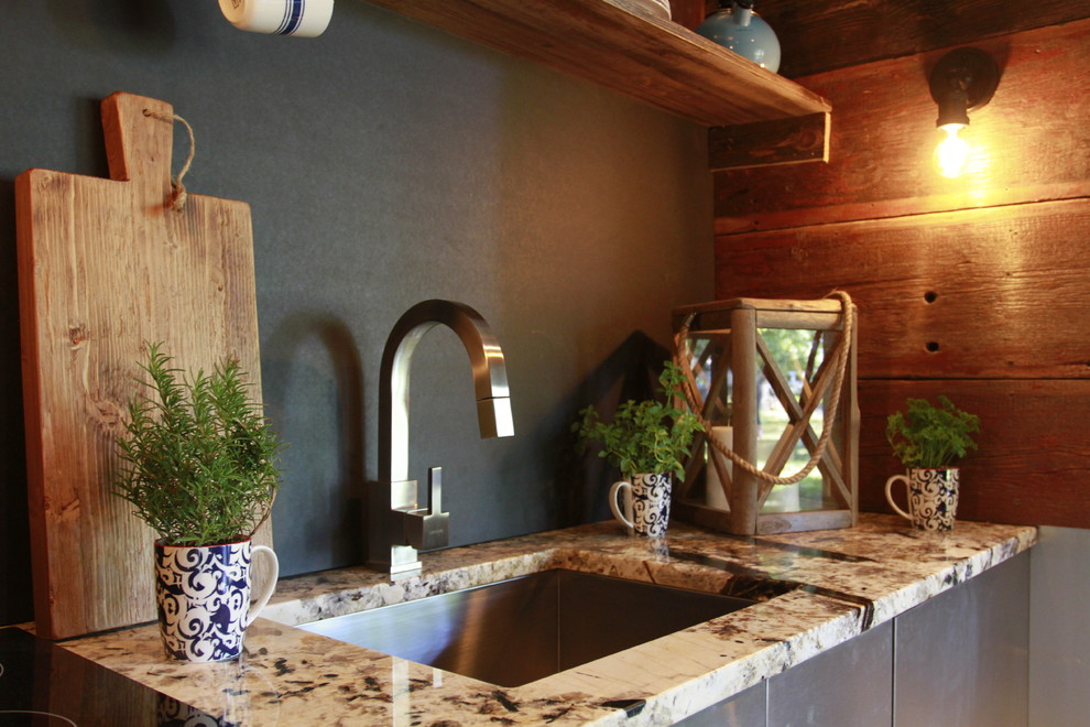 Inspiration for a small rustic single-wall light wood floor open concept kitchen remodel in Other with an undermount sink, flat-panel cabinets, stainless steel cabinets, granite countertops, black backsplash and no island