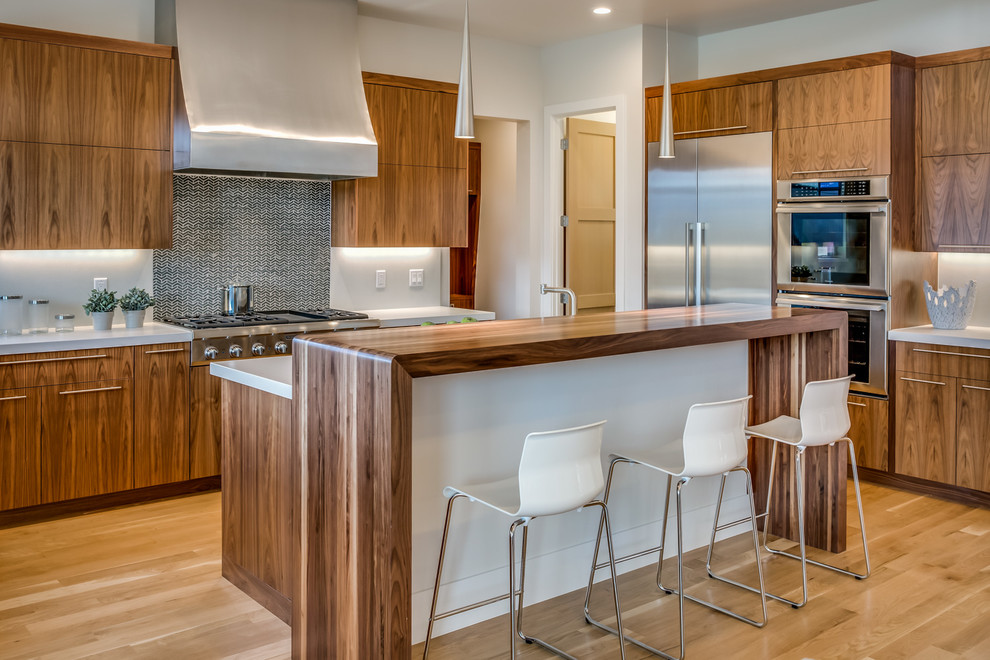 Moderne Küche in L-Form mit flächenbündigen Schrankfronten, hellbraunen Holzschränken, Küchengeräten aus Edelstahl, braunem Holzboden und Kücheninsel in Denver