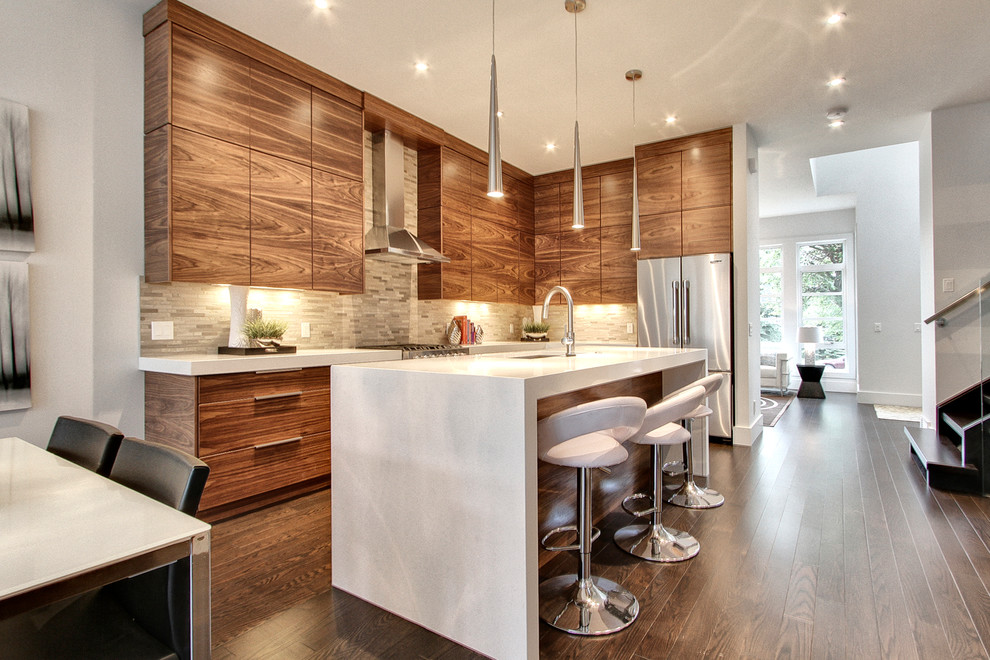 Bild på ett mellanstort funkis kök, med en dubbel diskho, släta luckor, skåp i mellenmörkt trä, bänkskiva i kvartsit, grått stänkskydd, stänkskydd i stenkakel, rostfria vitvaror, mörkt trägolv, en köksö och brunt golv