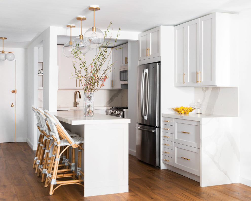 Immagine di una cucina classica con ante in stile shaker, ante bianche, paraspruzzi bianco, elettrodomestici in acciaio inossidabile, pavimento in legno massello medio, pavimento marrone e top bianco