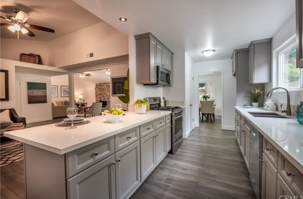 Small transitional galley gray floor open concept kitchen photo with a double-bowl sink, recessed-panel cabinets, gray cabinets, stainless steel appliances, a peninsula and white countertops