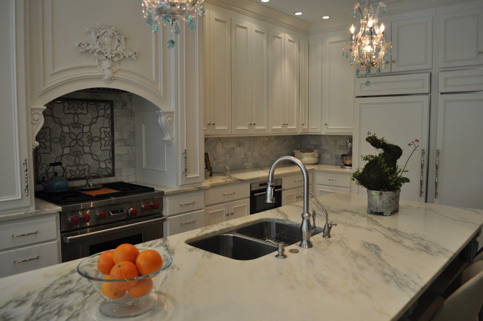 Open concept kitchen - large traditional l-shaped travertine floor and beige floor open concept kitchen idea in Miami with recessed-panel cabinets, marble countertops, white backsplash, stone tile backsplash, an island, an undermount sink, white cabinets, paneled appliances and white countertops