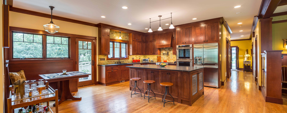 Cette image montre une cuisine ouverte craftsman en L et bois brun de taille moyenne avec un évier encastré, un placard à porte shaker, un plan de travail en stéatite, une crédence verte, une crédence en céramique, un électroménager en acier inoxydable, parquet clair, îlot, plan de travail noir, un sol marron et un plafond en papier peint.