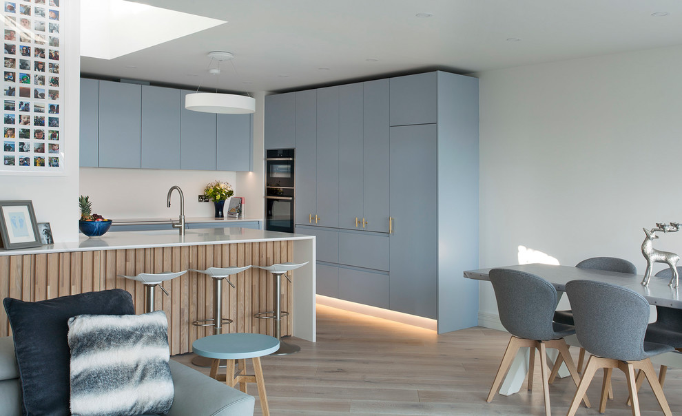 Medium sized scandinavian l-shaped kitchen/diner in Other with louvered cabinets, blue cabinets, quartz worktops, white splashback, stainless steel appliances, light hardwood flooring, an island and white worktops.
