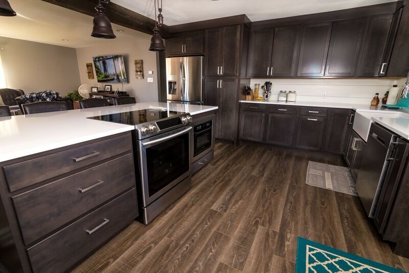 Large country l-shaped medium tone wood floor and brown floor eat-in kitchen photo in Denver with a farmhouse sink, shaker cabinets, dark wood cabinets, solid surface countertops, white backsplash, stainless steel appliances and an island