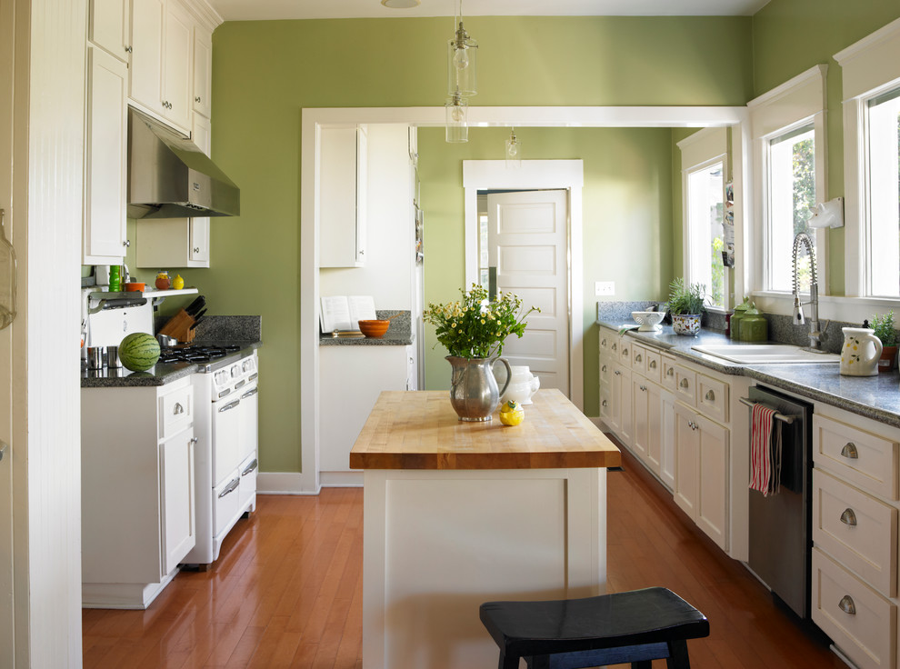 Zweizeilige Klassische Küche mit weißen Schränken, Kücheninsel, Einbauwaschbecken, Schrankfronten im Shaker-Stil, Küchengeräten aus Edelstahl und braunem Holzboden in Los Angeles