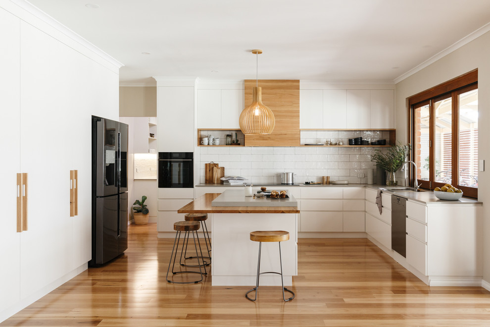 アデレードにあるコンテンポラリースタイルのおしゃれなキッチン (アンダーカウンターシンク、フラットパネル扉のキャビネット、白いキャビネット、白いキッチンパネル、白い調理設備、無垢フローリング、ベージュの床) の写真