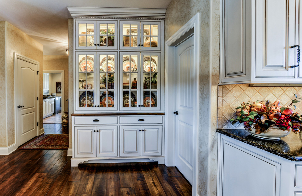 Inredning av ett klassiskt stort kök, med en rustik diskho, luckor med upphöjd panel, vita skåp, granitbänkskiva, beige stänkskydd, stänkskydd i stenkakel, rostfria vitvaror, mörkt trägolv och en köksö