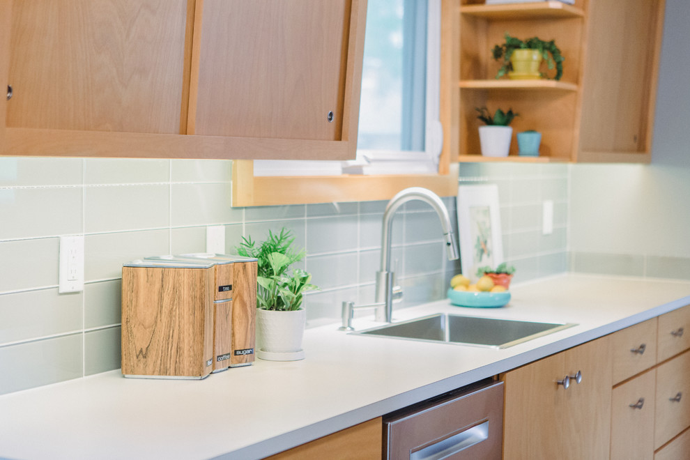 Small midcentury galley enclosed kitchen in Grand Rapids with a built-in sink, flat-panel cabinets, light wood cabinets, laminate countertops, grey splashback, glass tiled splashback, stainless steel appliances, medium hardwood flooring, no island, grey floors and beige worktops.