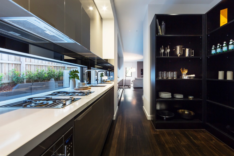 Inredning av ett modernt mellanstort linjärt kök med öppen planlösning, med en enkel diskho, släta luckor, svarta skåp, fönster som stänkskydd, integrerade vitvaror, mörkt trägolv och brunt golv