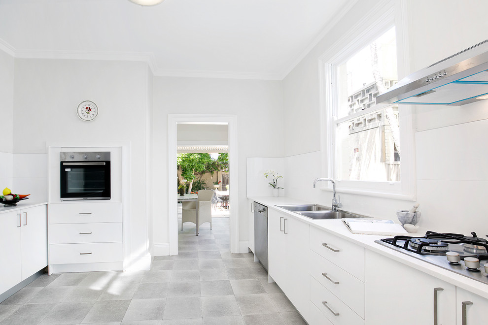 Inspiration for a medium sized traditional galley enclosed kitchen in Sydney with a double-bowl sink, flat-panel cabinets, white cabinets, composite countertops, white splashback, porcelain splashback, stainless steel appliances, lino flooring, no island, grey floors and white worktops.