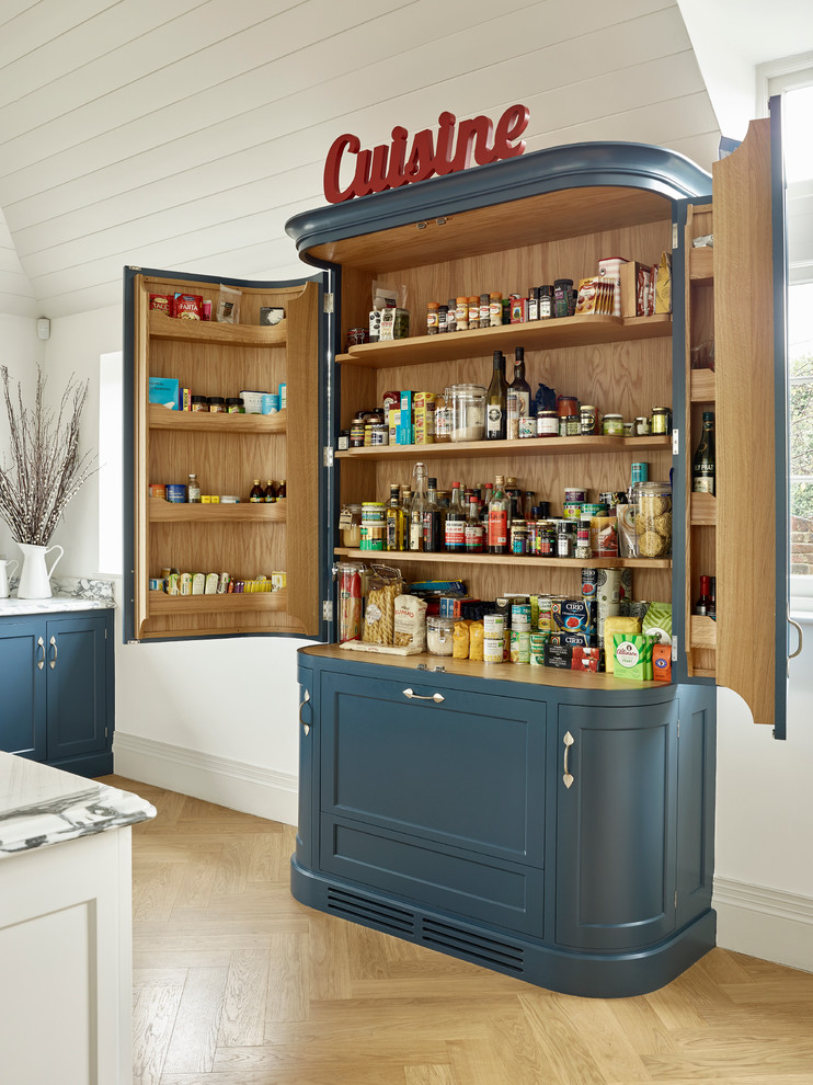Modelo de cocina campestre con despensa, armarios con paneles empotrados, puertas de armario azules y suelo de madera clara