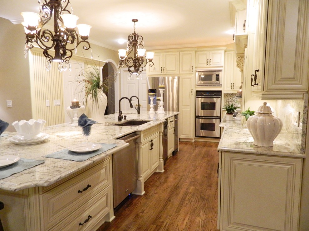 Enclosed kitchen - mid-sized traditional l-shaped dark wood floor and brown floor enclosed kitchen idea in Atlanta with a double-bowl sink, raised-panel cabinets, white cabinets, granite countertops, gray backsplash, stone slab backsplash, stainless steel appliances and an island