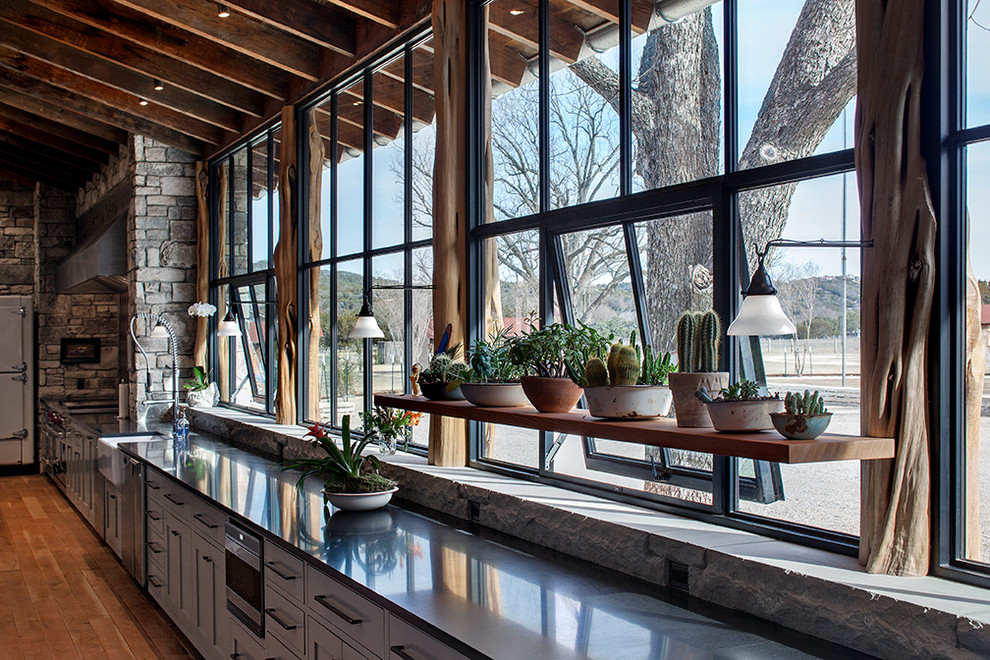 Immagine di una cucina stile rurale con lavello stile country, ante grigie, elettrodomestici in acciaio inossidabile e pavimento in legno massello medio