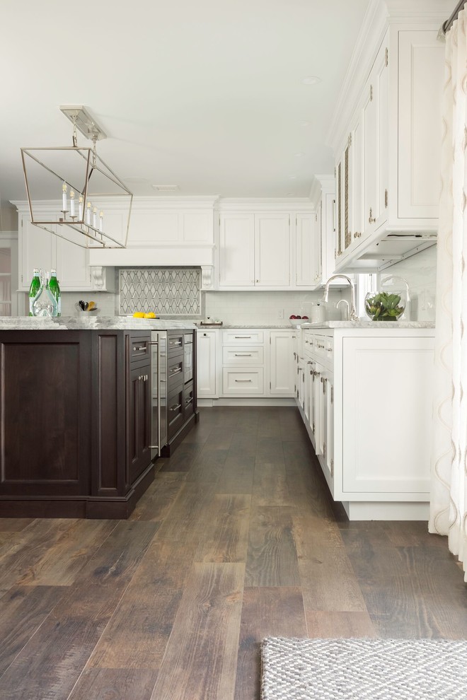 Large transitional u-shaped medium tone wood floor and brown floor enclosed kitchen photo in New York with a farmhouse sink, shaker cabinets, white cabinets, granite countertops, white backsplash, stainless steel appliances, an island and gray countertops