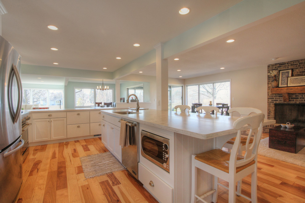 Example of a transitional l-shaped eat-in kitchen design in Grand Rapids with shaker cabinets, white cabinets, solid surface countertops, green backsplash and stainless steel appliances