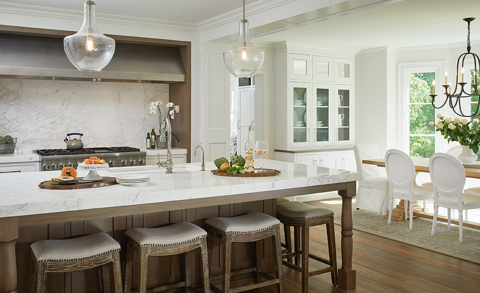Example of a large classic l-shaped medium tone wood floor eat-in kitchen design in Grand Rapids with a farmhouse sink, beaded inset cabinets, white cabinets, marble countertops, white backsplash, marble backsplash, paneled appliances and an island