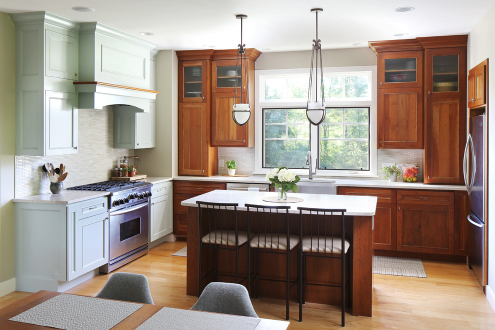 Example of an arts and crafts u-shaped medium tone wood floor and brown floor eat-in kitchen design in Grand Rapids with a farmhouse sink, recessed-panel cabinets, medium tone wood cabinets, gray backsplash, mosaic tile backsplash, stainless steel appliances, an island and white countertops