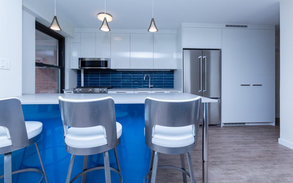 Пример оригинального дизайна: параллельная кухня среднего размера в стиле модернизм с обеденным столом, врезной мойкой, плоскими фасадами, белыми фасадами, столешницей из кварцевого агломерата, синим фартуком, фартуком из керамической плитки, техникой под мебельный фасад, деревянным полом, островом, бежевым полом и серой столешницей