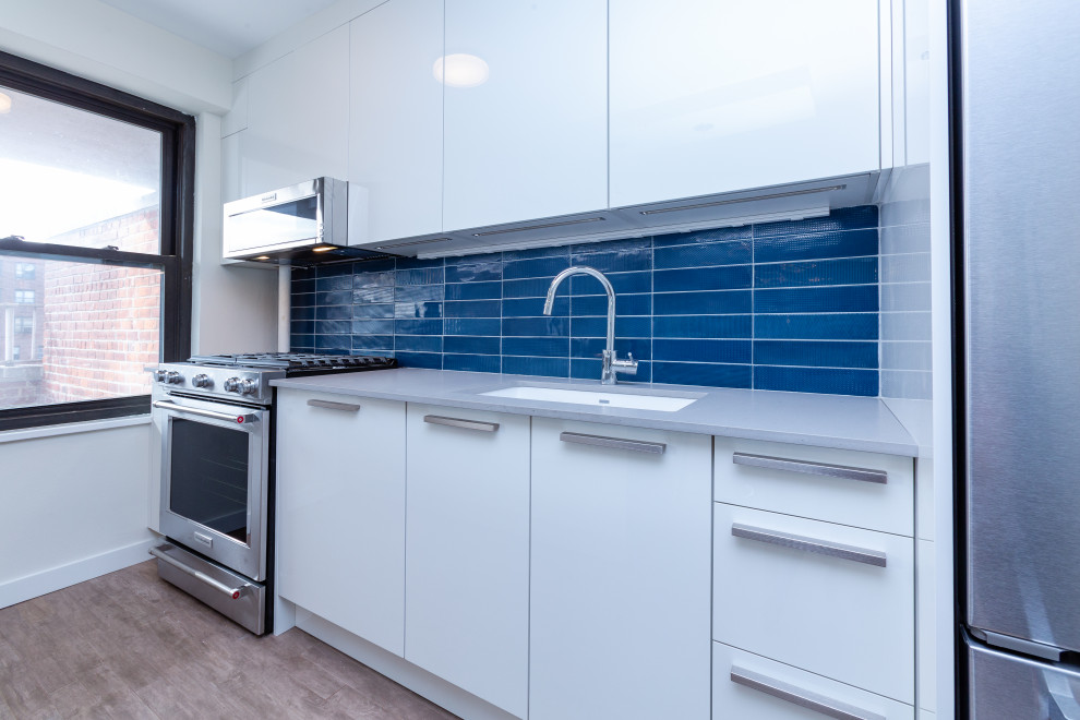 Idéer för att renovera ett mellanstort funkis grå grått kök, med en undermonterad diskho, släta luckor, vita skåp, bänkskiva i kvarts, blått stänkskydd, stänkskydd i keramik, integrerade vitvaror, målat trägolv, en köksö och beiget golv