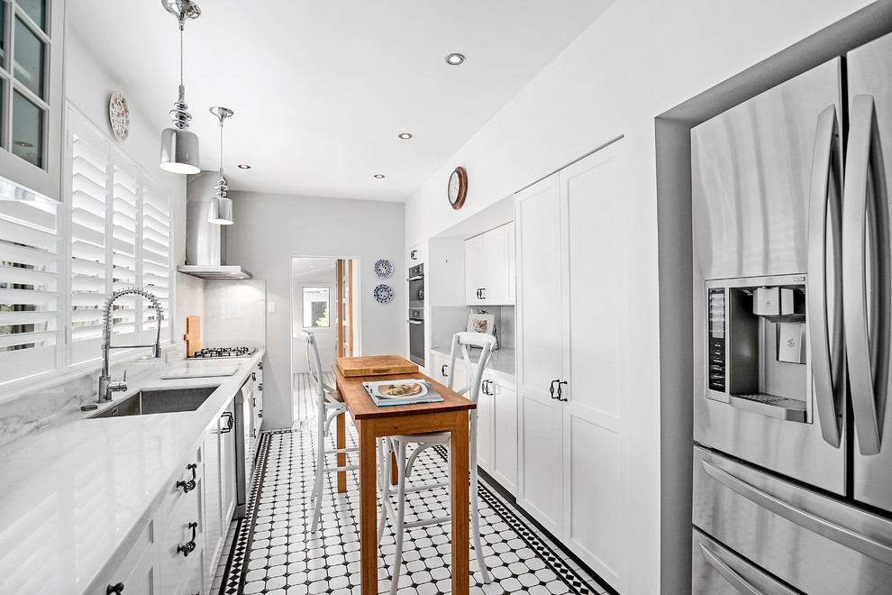 Inredning av ett klassiskt avskilt, mellanstort vit vitt kök, med en undermonterad diskho, luckor med infälld panel, vita skåp, bänkskiva i koppar, stänkskydd i marmor, rostfria vitvaror, klinkergolv i keramik, en köksö, vitt stänkskydd och vitt golv